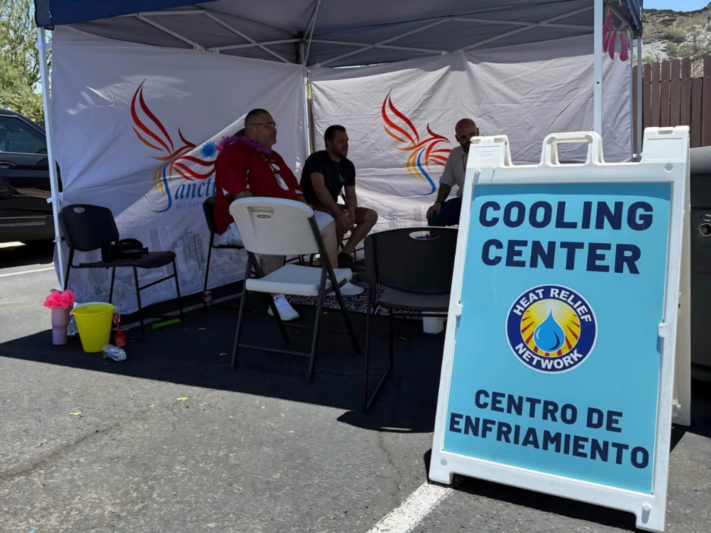 Sanctuary team members seated under a cooling center tent with a bilingual Heat Relief Network sign during summer outreach in Phoenix