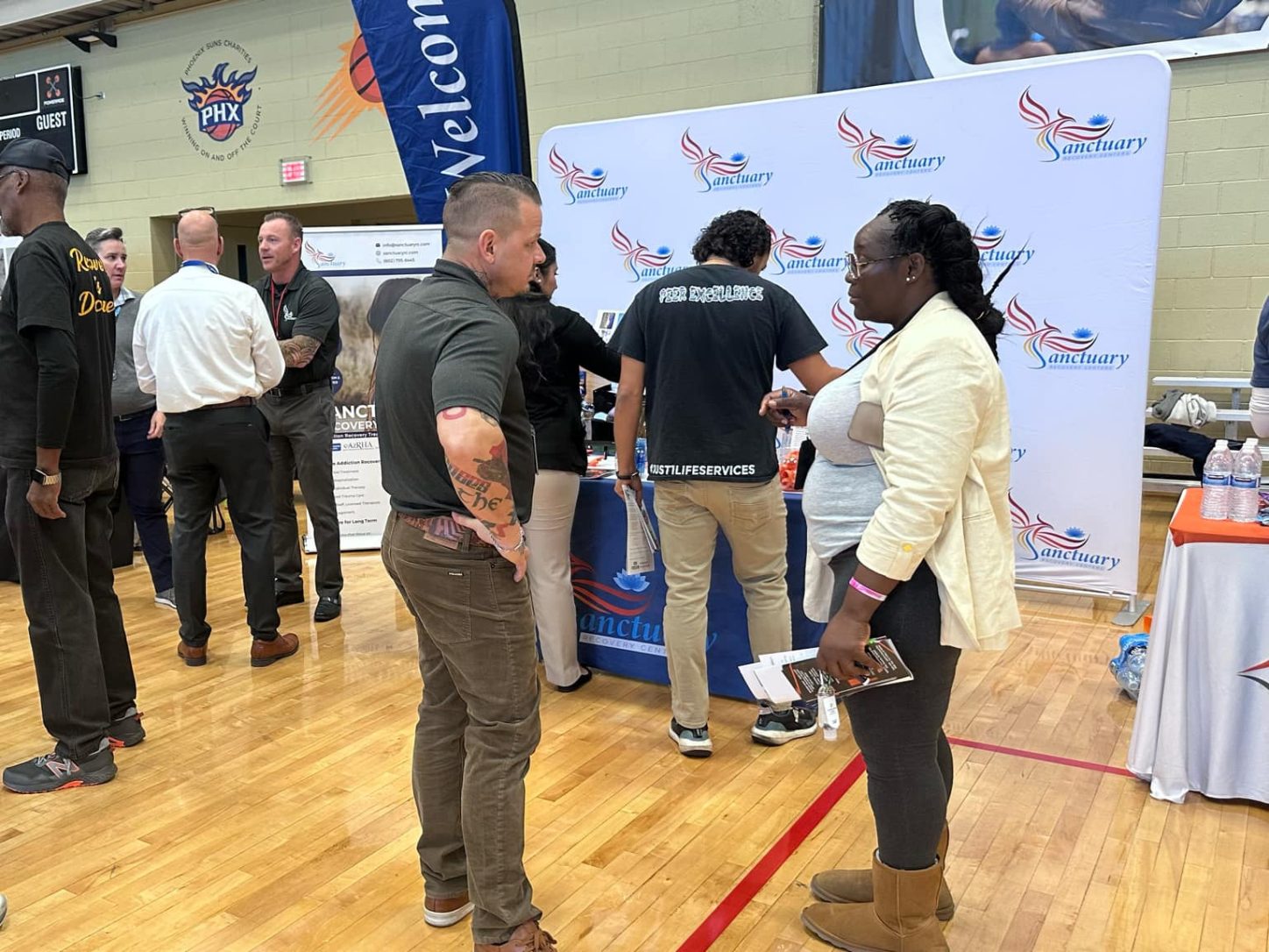 Neighbors and staff talking at the Sanctuary booth during a community resource fair in a school gym